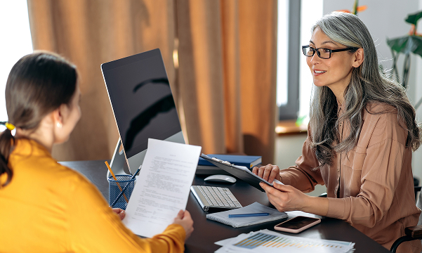 A new employee meets with a plan representative at a desk, reviewing paperwork during an office conversation.